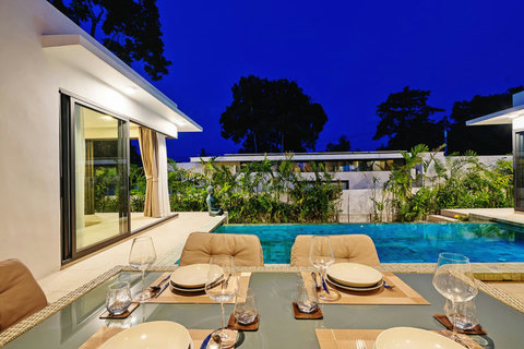 Romantic poolside dining setup at dusk with sun loungers and illuminated pool