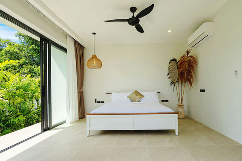 King bedroom with ceiling fan and garden views through floor-to-ceiling glass
