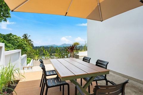Outdoor dining area with wooden table and chairs surrounded by tropical gardens at Villa Ombra