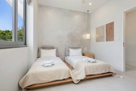 Wake up in this serene bedroom with plenty of natural light, two cozy single beds dressed in fresh white linens, and a peaceful tropical garden view.