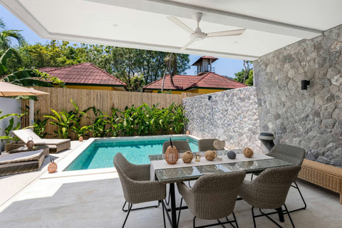 Relax in the shade of this covered seating area overlooking the pool. The stone wall and wicker seating create a calm tropical escape.