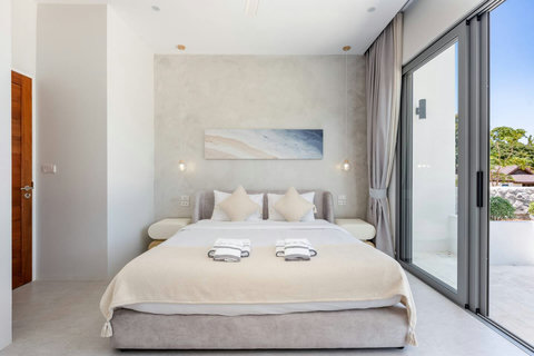 Sink into luxurious white linens in this serene bedroom. Soft pendant lights and outdoor access create a peaceful retreat.