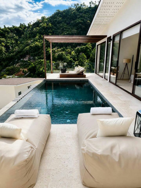 “Relax on sun loungers beside the infinity pool, surrounded by lush tropical greenery and sea breeze”