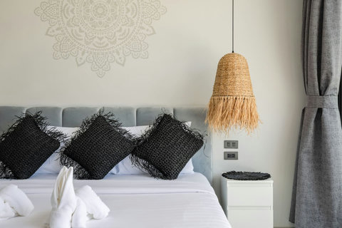 Grey upholstered bed with dark cushions and woven bedside lighting