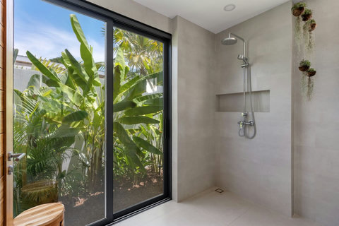Walk-in rain shower beside full-height glass and tropical greenery
