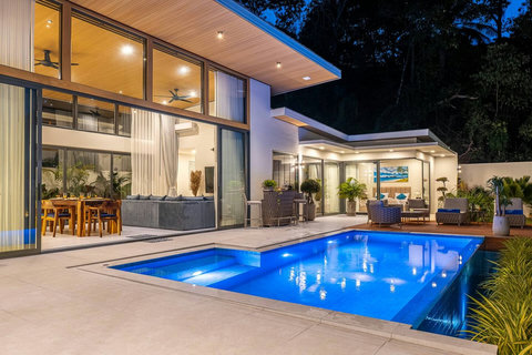 Modern luxury villa featuring indoor-outdoor living and poolside dining at night.