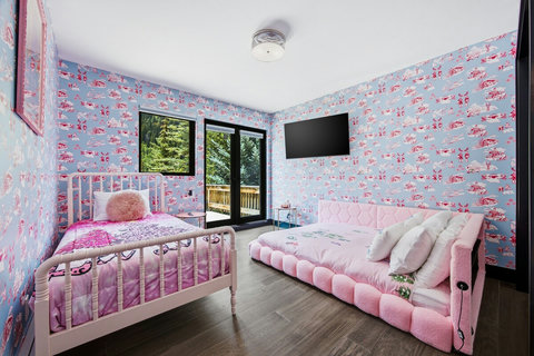 Whimsical pink bedroom with daybed, smart TV, and serene forest views.