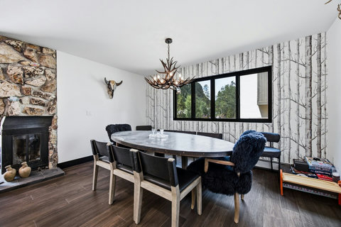 Cozy dining room with stone fireplace, large table, and wooded views