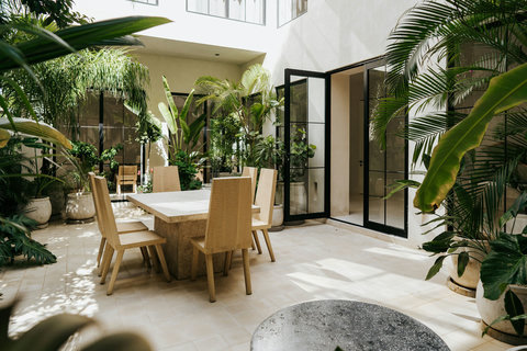 Bright, open-air courtyard featuring a long dining table set, surrounded by abundant tropical foliage