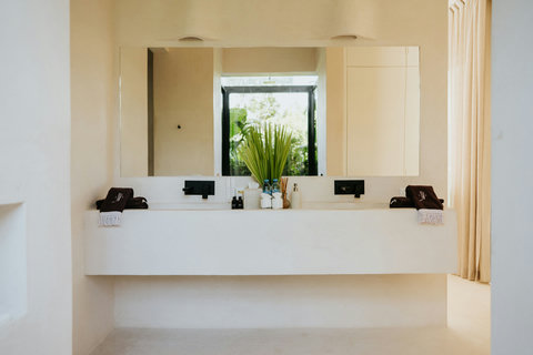 Clean, minimalist bathroom with a spacious trough sink, a wide mirror and thoughtful amenities