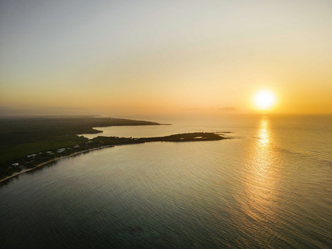 HOTEL VIEWS -Sun melts into coral horizon, gilding water and distant island, bathing evening in gentle amber hush.
