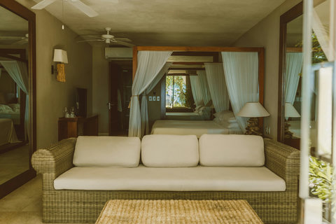 WATERFRONT SUITES - Interior palette echoes coast, rattan sofa and mirrored panels reflecting dappled light and distant sea glimmer.