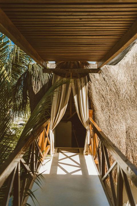 Sunlight filters through slatted roofs onto a private path leading toward serene, thatched sanctuary spaces.
