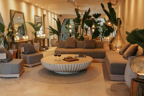 LOUNGE AREA - Interior lounge murmurs softly; chessboard waits, two glasses breathing dark fruit while ceiling fans whisper slow moves.