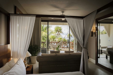 WATERFRONT SUITES - Upstairs retreat opens to leafy canopy and open horizon, ceiling fan murmuring while palms stir distant salt light.