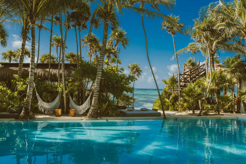 Twin hammocks sway over mirrored water; trade-winds carry soft surf murmur, framing a perfectly idle midday ritual.