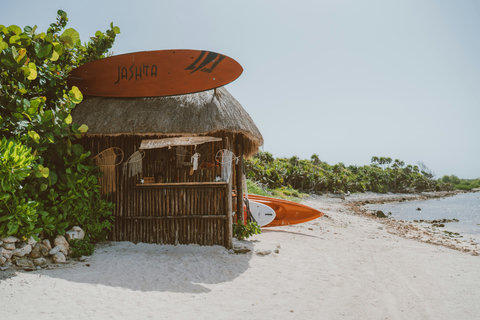 ADVENTURE SHACK - Sunlight warms the white sand beside a thatched shack, where vibrant kayaks rest, waiting for exploration.