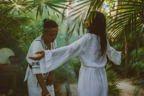 A cleansing ritual unfolds amidst lush greenery, connecting spirit and nature through gentle smoke and touch.