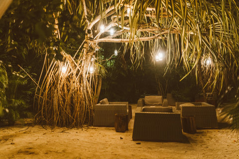 Night garden flickers; glass lanterns hang like fireflies above woven chairs, sand cooling between wandering toes.