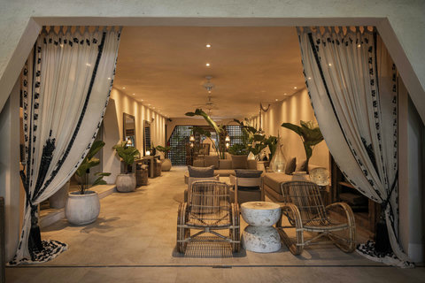 Wide curtains gather, revealing lounge ready for dusk; rattan rockers and silver lamps promise long gentle conversations.