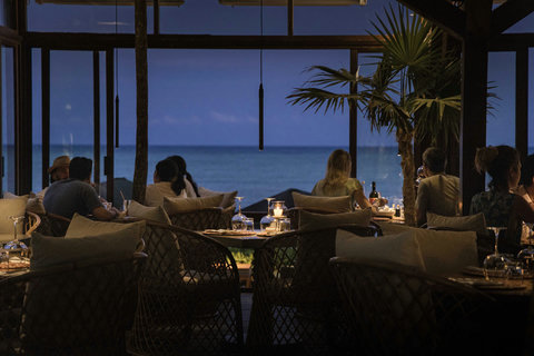 As dusk falls, candlelit tables glow warmly against the deep blue horizon, framing an evening of shared stories.
