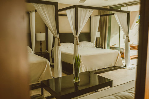 SUPERIOR DOUBLE DELUXE SUITES -Gaze through parted curtains at twin beds framed in dark wood and soft linen, where a single green stem on glossy black table anchors the room in calm, curated stillness.