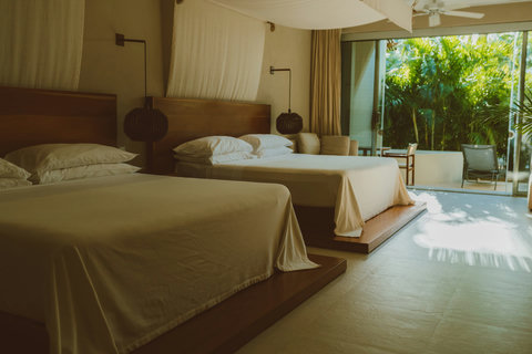Rest beneath woven pendant lights that cast gentle shadows over plush platforms, while glass doors open to sunlit stone and leafy privacy just beyond your barefoot reach.