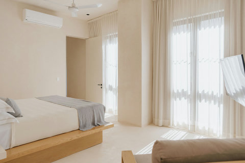 Sunlit bedroom with an armchair, air conditioning, and expansive floor-to-ceiling views