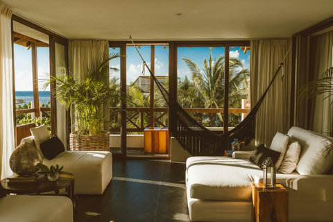 Sway gently in the hammock strung between sunlit windows, surrounded by woven baskets, leafy palms, and white linen sofas that invite you to dissolve into the day’s last golden hush.