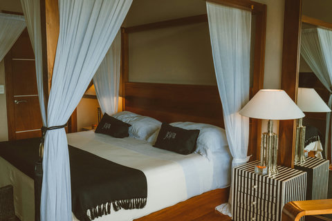 Allegra Deluxe Suite - Sink into bed framed by flowing veils and tactile throws, where black-and-white linens contrast with glowing lamps and the air carries the faint salt-kissed breeze from just outside your window.