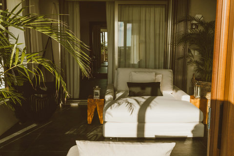 Lounging becomes ritual here white linen cradles you beside raw-edge side tables, while palm shadows stretch across stone and hammocks sway just beyond open doors.