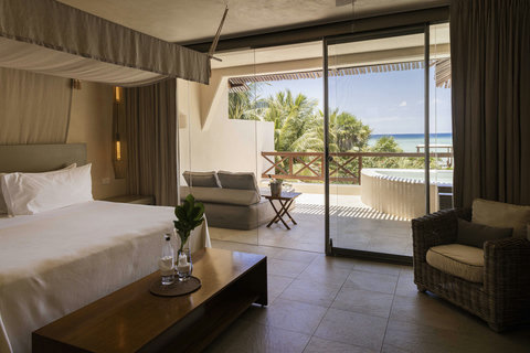 SUITE - Step from bed to terrace where sunlight pools on stone, inviting you to sink into outdoor seating beside a private tub all framed by swaying palms and horizon-hugging calm.