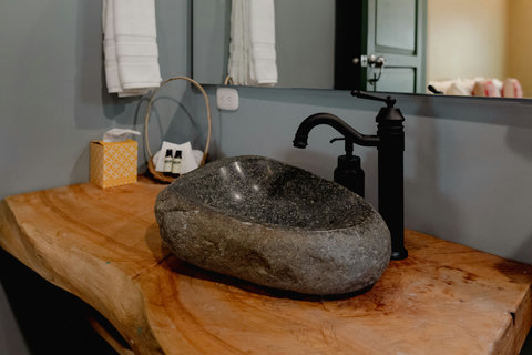 BATHROOM Immerse yourself in rustic elegance where nature meets luxury! This artisan-crafted stone sink with warm wood accents sets the tone for a serene and rejuvenating getaway. Let the soft lighting and thoughtful amenities envelop you in comfort durin