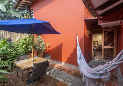 Patio - Step into your private oasis where sunlight dances on terracotta walls and a gentle breeze invites you to unwind in the cozy hammock. Savor your morning coffee al fresco under the shade of a vibrant blue umbrella, surrounded by lush greenery that