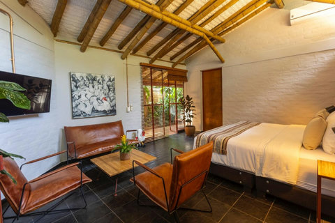 Bedroom 1 - Bask in the serene glow of this tropical retreat, where bamboo accents and natural light create a warm, inviting sanctuary. Relax in leather chairs, enjoy modern amenities, and let the lush greenery just beyond your window envelope you in tran