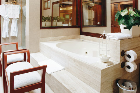 Tub Area - Unwind in luxury as natural light streams through the windows, illuminating your private spa retreat. Sink into the inviting warmth of the marble tub, surrounded by lush greenery and plush amenities, for a truly rejuvenating escape.