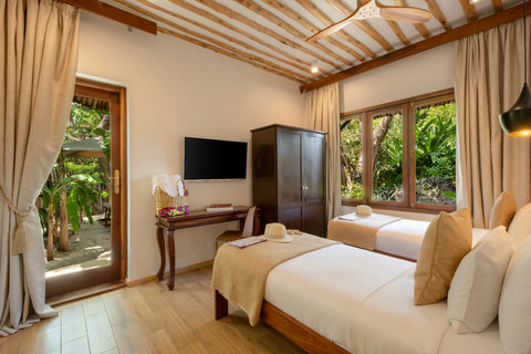 As evening settles, two beds, pale textures, and leafy views make sharing the space feel easy and beautifully quiet.