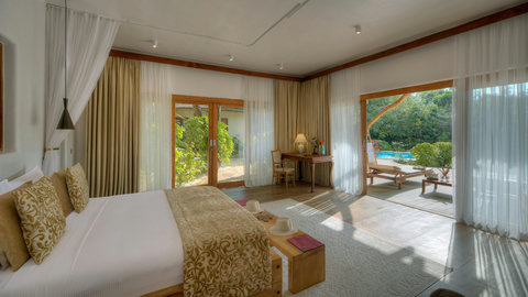 Evening begins in the bedroom with sheer curtains, low light, and the pool shimmering just beyond the terrace.