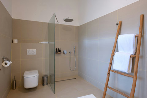 The bathroom keeps the same calm, pale stone, warm water, and space for an unhurried reset.