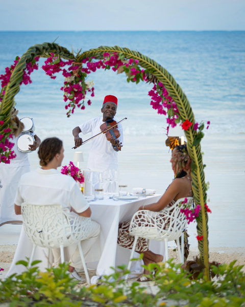 By evening, dinner arrives with flowers, music, and candlelight, the sea nearby and every conversation glowing a little longer.