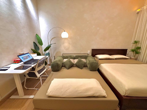 Spacious two sleeping areas: a queen bed and a queen sofa bed (160cm x 200cm), providing comfortable accommodations for up to 4 guests. Green decorative cushions enhance the sofa, while a functional work desk is positioned nearby