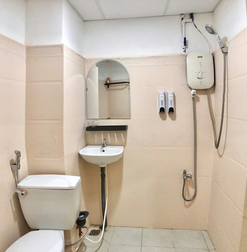 Compact bathroom featuring a shower with a water heater, a modern toilet, and a sink with a round mirror above it. Two dispensers for soap and shampoo are mounted on the wall, providing convenience for guests during their stay.