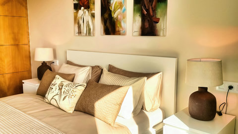 Sunlit modern bedroom with plush bedding, art, and twin lamps