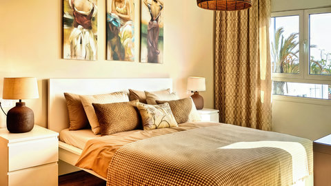 Sunlit, stylish bedroom with plush queen bed and palm-view windows