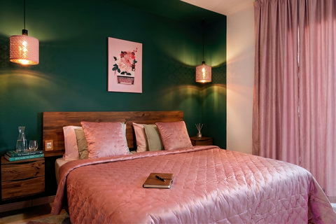Chic bedroom with emerald wall, blush bedding, and warm pendant lights