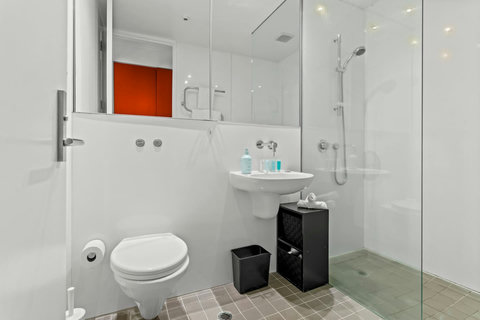 The bathroom has a wash sink, glass shower and toilet plus a large mirror.