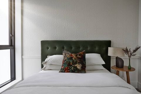 The forest green headboard and matching cushion  are beautiful against the white walls and sheets.