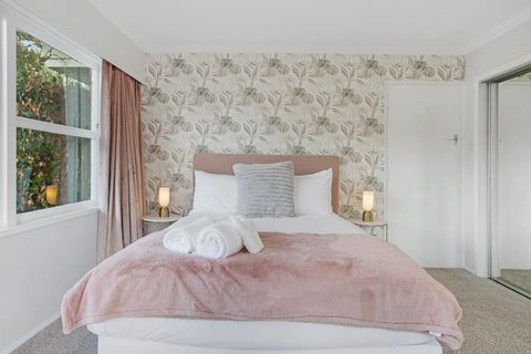 This bedroom has a feminine feel with patterned wallpaper and pink throw.