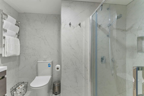 The bathroom has a glass shower box, vanity unit and toilet.