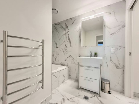 The bathroom has a built-in tub, a large mirror, a vanity and a heated towel rail.